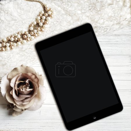 tablet ipad with blank screen and pearls on a white wooden background. Elegant reading mockup