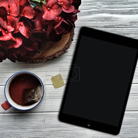 Foto de Tableta y té para leer maqueta con hortensias rojas - Imagen libre de derechos