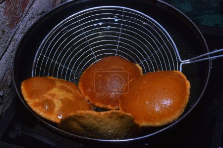 Téléchargez les photos : Chapati friture (poori) avec cuillère sur poêle, huile bouillante dans une poêle avec fond sombre, concept de cuisine - en image libre de droit