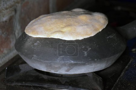 Foto de Manos de una ama de casa india mientras hornea pan (chapati) en una olla de tierra usando gas GLP - Imagen libre de derechos