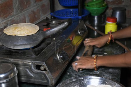 Foto de Manos de una ama de casa india mientras hornea pan (chapati) en una olla de tierra usando gas GLP - Imagen libre de derechos