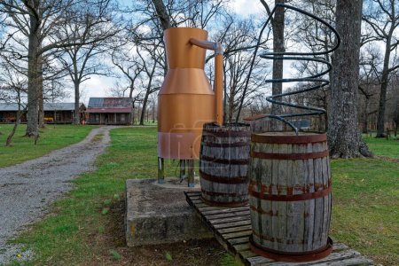 A reproduction of an old moonshine still with wooden barrels and a copper tank on display in front of an old rustic homestead in Tennessee