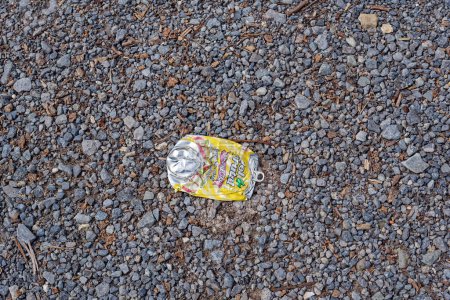 Foto de Un refresco o jugo brillante y colorido puede aplanarse en el suelo en la vista de primer plano del estacionamiento de grava con espacio para copiar - Imagen libre de derechos