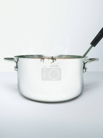 Close-up of a stainless steel pot with spoon and tomato sepals hanging out of the edge