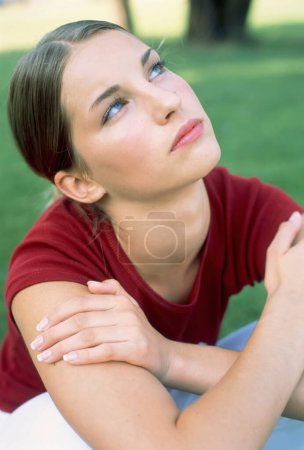 Teenage girl sitting outside looking up with a pensive expression