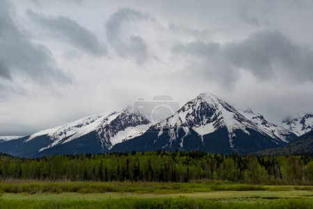 Blick auf schneebedeckte Berggipfel mit Wäldern und Feuchtgebieten entlang der Fahrt von Terrance, Osten nach Prince George auf dem Highway 16 (Highway of Tears) an einem bewölkten Tag; British Columbia, Kanada