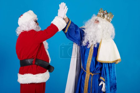 Photo for Santa Claus and a Wise Man high-fiving each other. Give my five on a blue background - Royalty Free Image