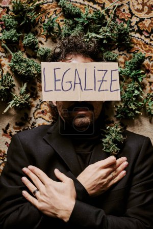 Téléchargez les photos : Un jeune cadre masculin entouré de bourgeons de marijuana et appelant à la légalisation du cannabis. Concept de drogue - en image libre de droit