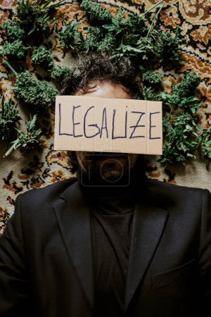 Téléchargez les photos : Un jeune cadre masculin entouré de bourgeons de marijuana et appelant à la légalisation du cannabis. Concept de drogue - en image libre de droit