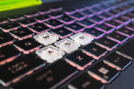 Highlighted gaming keys with pink purple gradient light and blurred background. Powerful dark notebook keyboard close-up. Tech, IT, e-sport, computer science background Poster 646768496