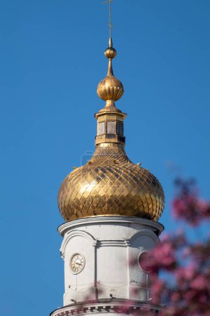 The Assumption or Dormition Cathedral golden dome, Orthodox church in pink trees blossom on blue sky. Sightseeing Ukrainian Baroque architecture style in spring Kharkiv, Ukraine