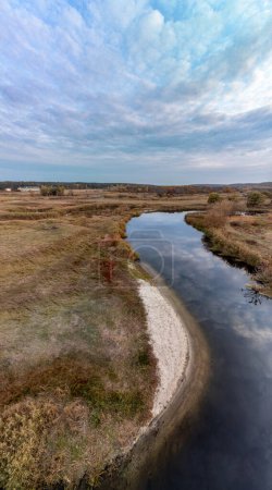 Aerial vertical panorama of blue river in autumn valley with cloudy sky