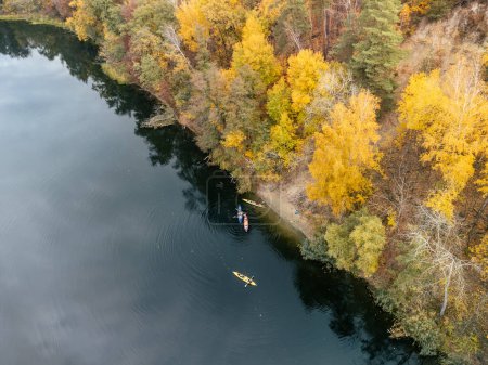 Aerial river with kayaks rowing on calm water near colorful autumn forest riverbanks Siverskyi Donets River in Ukraine