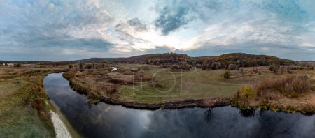 Aerial sunset panorama on river curve in autumn with reeds, trees, dirt road and cloudy skyscape. Siverskyi Donets River in Ukraine