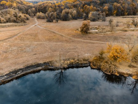 Aerial riverside in autumn golden yellow valley with dirt road. Siverskyi Donets River in Ukraine rural landscape