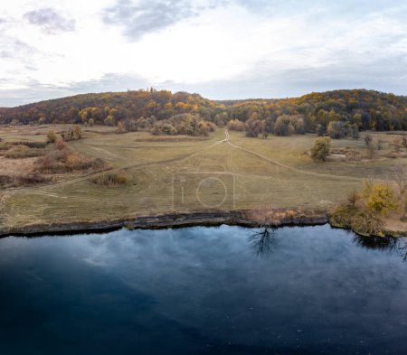 Aerial river shore in autumn valley with dirt road and epic cloudy sky in Ukraine