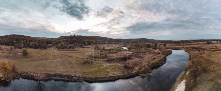 Aerial panorama on river curve in autumn valley with reeds, dirt road and epic cloudy sky in Ukraine