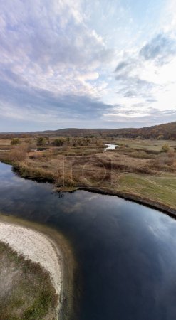 Aerial vertical panorama on blue river curve in autumn with cloudy skyscape