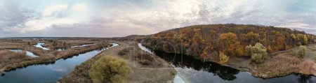 Aerial wide panorama on river curve in autumn valley with reeds, trees and epic cloudy sky in Ukraine