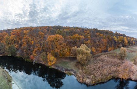 Aerial panorama of river shore near autumn forest and grey cloudy sky in Ukraine