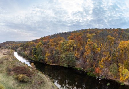 Flusskurve im Herbstwald mit grauem bewölkten Himmel. Gehölztes Flussufer in launiger Herbstluft