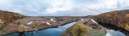 Aerial trees growing on river curve panorama with autumn forest and scenic cloudy sky in Ukraine