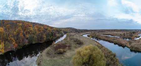 Aerial trees on river curve panorama with autumn forest and grey cloudy sky in Ukraine