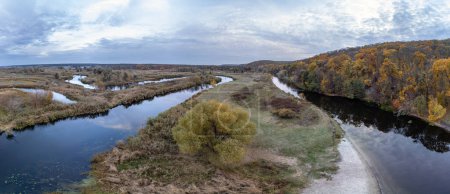 Aerial tree growing on river curve panorama with autumn forest and grey cloudy sky in Ukraine