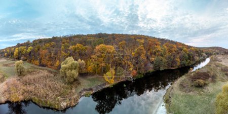 Aerial trees growing on riverside, panorama with autumn forest and scenic cloudy sky in Ukraine