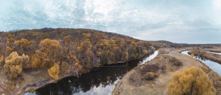 River curve in golden autumn forest with grey cloudy sky. Wooded riverbanks in autumnal aerial