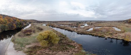 Aerial autumn trees on river curve panorama with forest and cloudy sky in Ukraine