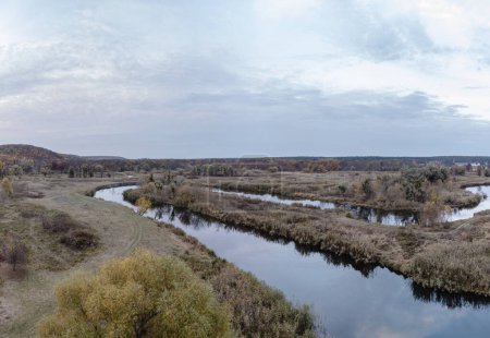 Aerial dirt road on Siverskyi Donets river coast with autumn forest and cloudy sky in Ukraine