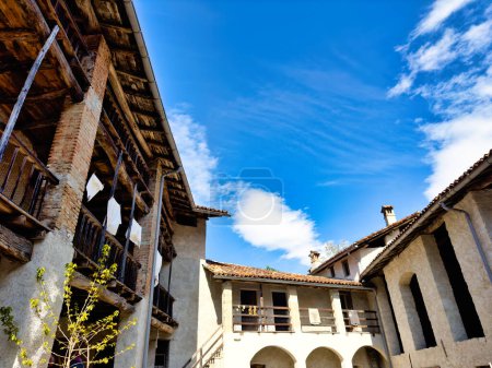 Traditionelles europäisches Bauernhaus mit offenem Hof, mit mehreren Ebenen von Balkonen, Sichtbalken und alten hölzernen Bauernkarren, die vor einem strahlend blauen Himmel stehen