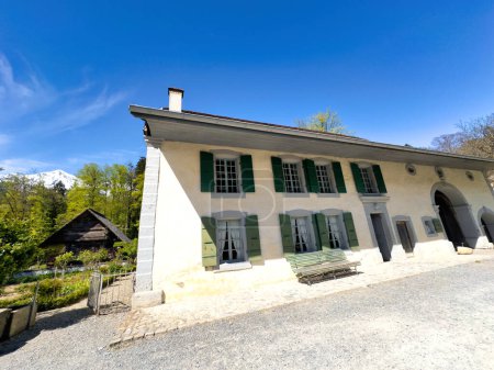Casa suiza clásica con persianas verdes y un pintoresco telón de fondo de montaña nevada, situada en un entorno sereno con un cielo azul claro