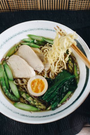 A bowl of noodles with chicken, asparagus, and green vegetables