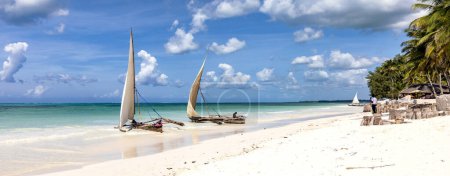 Téléchargez les photos : Spectacles traditionnels sur une plage sur la côte de Zanzibar. Bateaux dans l'océan turquoise et ciel bleu, panorama. - en image libre de droit