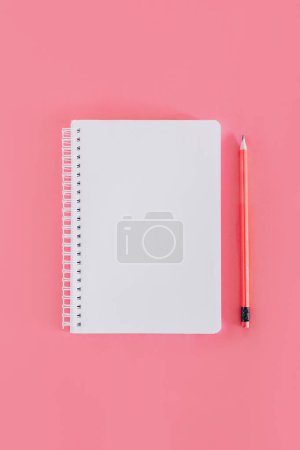 Foto de Cuaderno con una página en blanco y un lápiz sobre fondo rosa. Acostado. Lugar para el texto. - Imagen libre de derechos