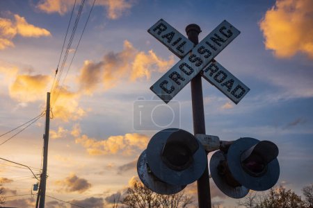 Téléchargez les photos : Un panneau d'avertissement de passage à niveau vintage, situé à Lambertville, NJ, se tait pendant un coucher de soleil avec des cumulus et des lignes électriques en arrière-plan. - en image libre de droit