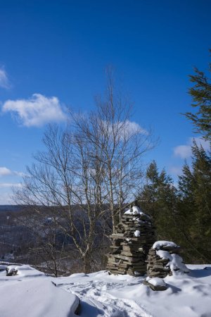 Photo for The Bouchoux Trail near Long Eddy NY is a 5.5-mile hiking path that hugs the Delaware River, photographed under a few inches of snow during the winter. Stone stacks at the ledge of a valley view. - Royalty Free Image
