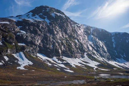 Téléchargez les photos : La neige a recouvert la vallée de Breiddalen au parc national de Jotunheimen en Norvège, le long de la route de Geiranger, pendant une journée d'été. Un camping-car stationné repose au pied de la montagne. - en image libre de droit