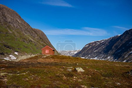Téléchargez les photos : La neige a recouvert la vallée de Breiddalen au parc national de Jotunheimen en Norvège, le long de la route de Geiranger, pendant une journée d'été. Une cabane repose près du pied d'une montagne. - en image libre de droit