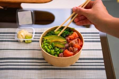 Téléchargez les photos : Poke bowl cru frash appétissant servi avec saumon, avocat, riz, salade d'algues avec edamame. Livraison de nourriture. Vue d'en haut. - en image libre de droit