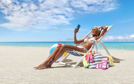 Foto de Mujer feliz en la playa en la tumbona de la playa, tomar el sol, utiliza el teléfono móvil, en un día soleado con cielo azul, concepto de vacaciones en la playa de verano, compras en línea, viajes de reserva, y alojamientos resorts - Imagen libre de derechos