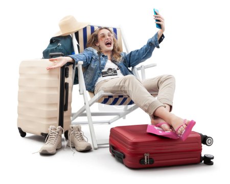 Foto de Mujer alegre feliz turista en traje de viaje, en la silla de cubierta con maletas de carro, hacer selfie con teléfono móvil. Vacaciones de verano en la playa, reserva de vuelos y vacaciones. Viajes influencer estilo de vida - Imagen libre de derechos