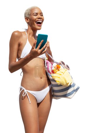 Foto de Mujer feliz en el lado de la playa con bikini sosteniendo una bolsa de playa y el uso de teléfono móvil, aislado sobre fondo blanco. Concepto de vacaciones en la playa de verano, compras en línea, reserva de viajes y resort - Imagen libre de derechos