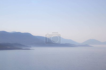View of the mountains and the sea. Beautiful mountain landscape in the hazy weather. Sunset and sea. Calm blue water and perfect seascape. Mountains and Albanian and Greece coastline view
