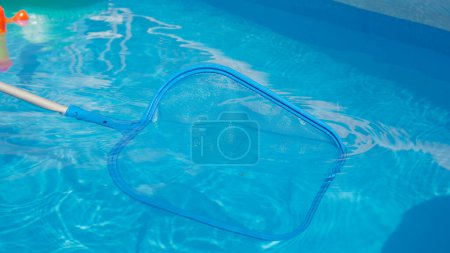Photo for CLOSE UP: Unrecognizable person is cleaning pool in the backyard. Pool cleaner uses a leaf net during seasonal maintenance works. Plastic pool skimmer cleans up tiny leaves from the glassy water. - Royalty Free Image