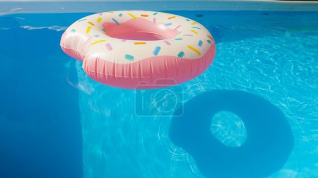 Photo for CLOSE UP: Colorful inflatable donut floats around the empty aqua colored pool in someone's backyard. Detailed shot of a plastic doughnut floatie drifting around the empty garden pool on a sunny day. - Royalty Free Image