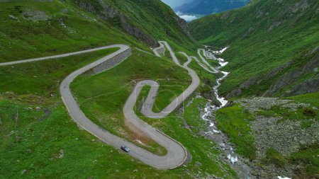 Photo for DRONE: Tourists on road trip across the mountains of Switzerland drive along hairpin turns of Gotthardpass. Grey colored tourist car cruises along the scenic switchback road of Passo San Gottardo. - Royalty Free Image