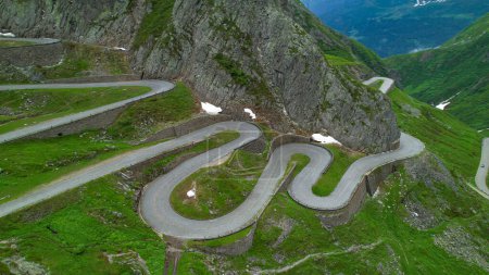 Foto de AERIAL: Volando por encima de un camino de horquilla serpenteando por las hermosas montañas suizas. Punto de vista Drone de una carretera de retorno vacía en Gotthardpass escénico, Suiza. Ruta de horquilla vacía en los Alpes. - Imagen libre de derechos